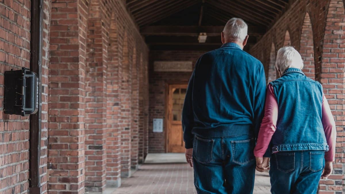 An elderly couple holding hands as they walk through a brick corridor, exuding love and companionship.