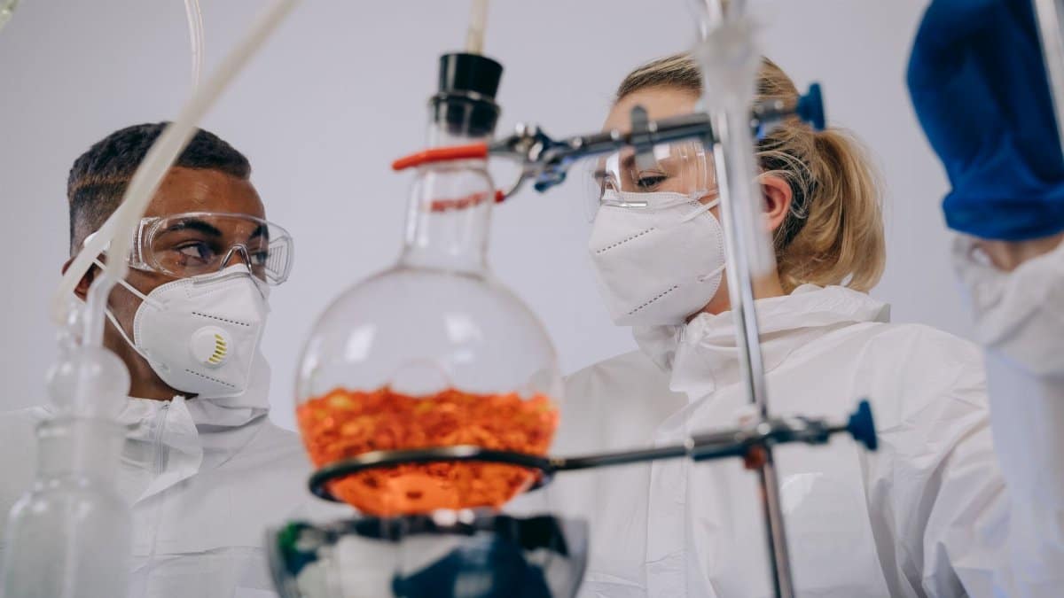 Two scientists in PPE conducting experiments with lab equipment, focusing on chemical reactions.