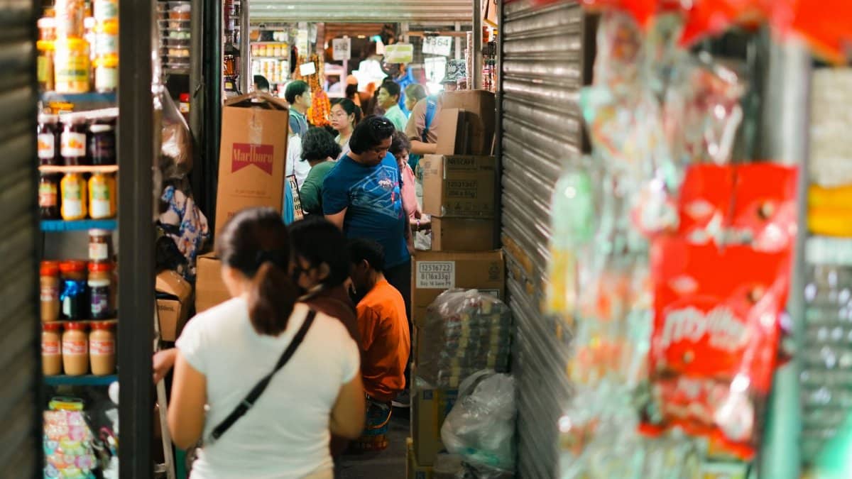 A crowded indoor market with people shopping and stocked shelves.