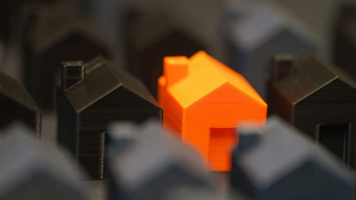 A vibrant orange model house stands out among black miniature houses, symbolizing real estate concepts.