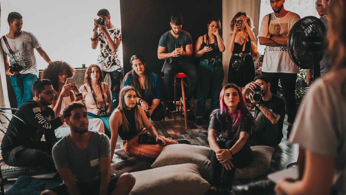Group of multiethnic young people wearing casual clothes gathering together in spacious studio and listening attentively to female speaker