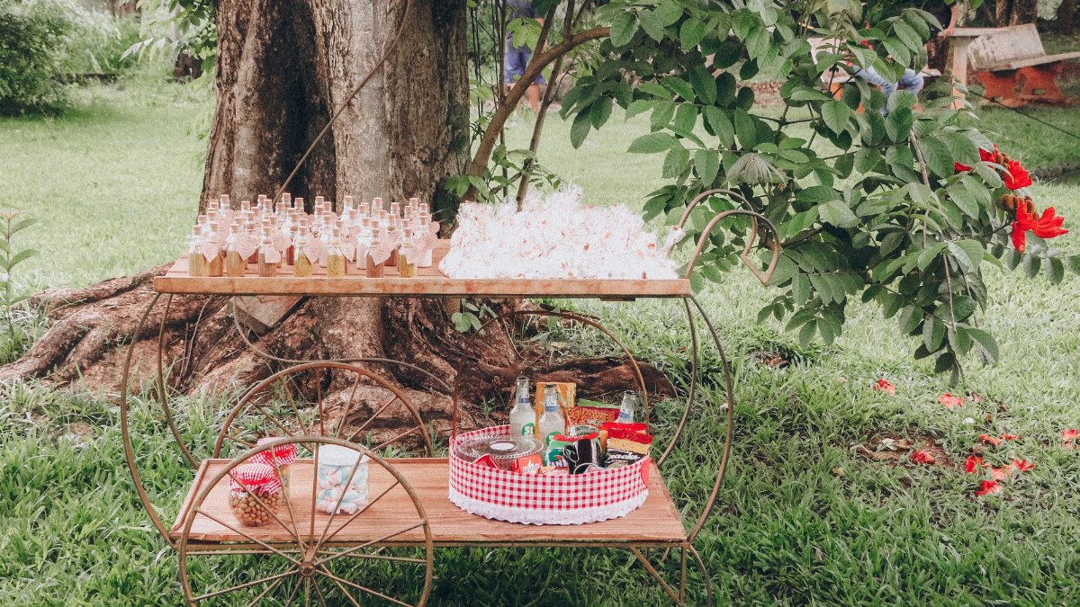 A rustic beverage cart set outdoors in a lush green garden, perfect for a summer picnic.