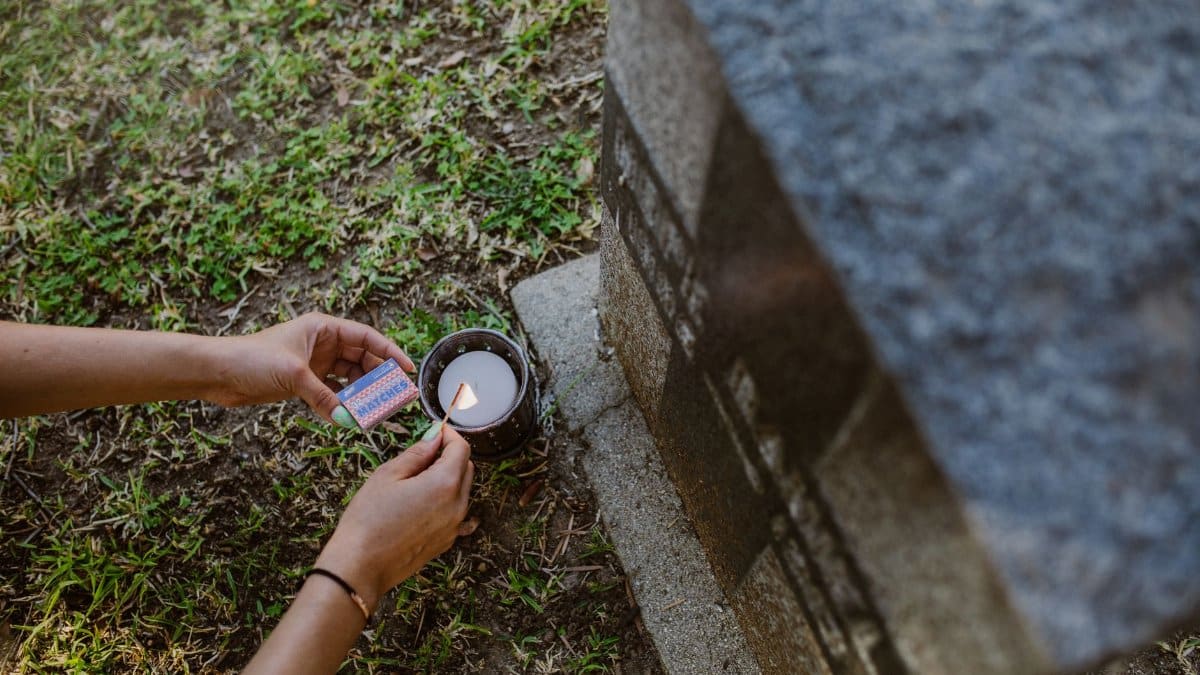Close-up of hands lighting a candle next to a tombstone in a cemetery.