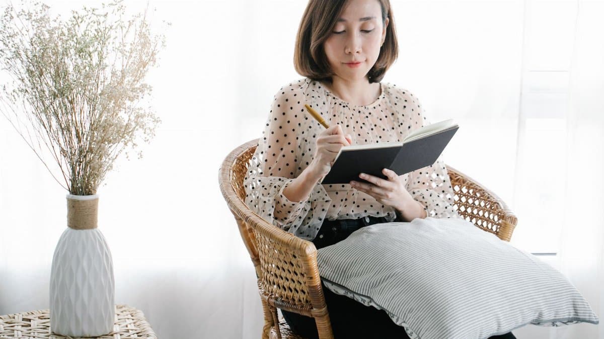 Woman sitting on a rattan chair writing in a notebook, creating a calm and introspective atmosphere.