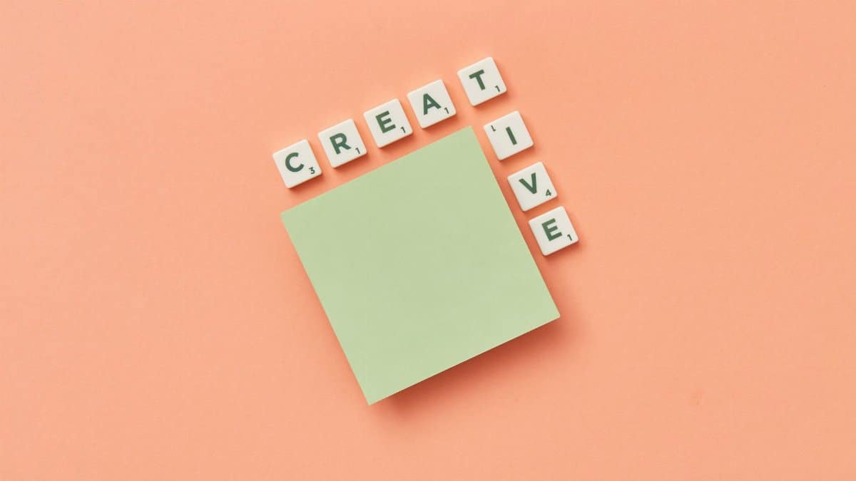 Minimalist creative concept with green sticky note and letter tiles on peach background.