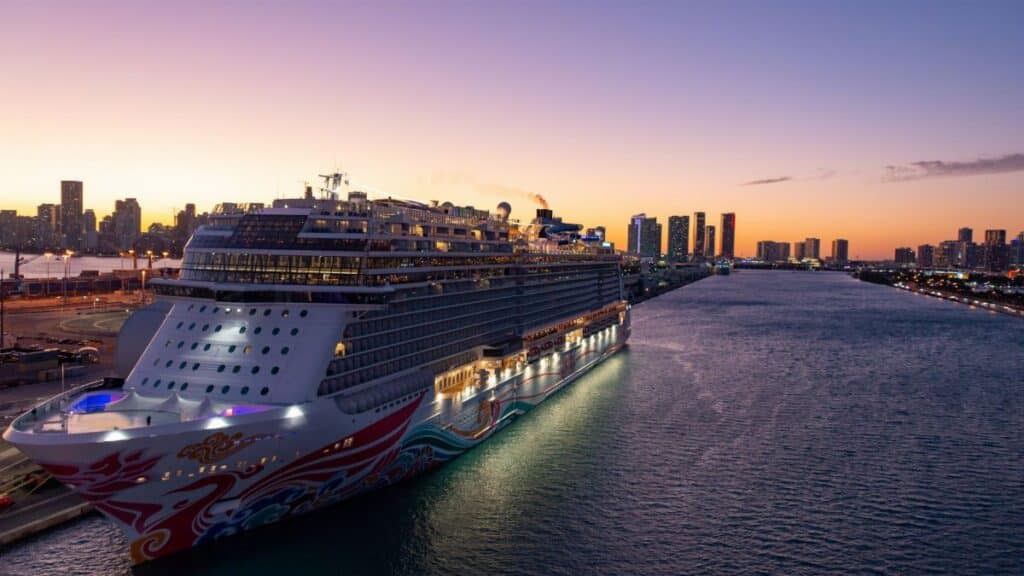 A luxury cruise ship docked in Miami Bay at sunset with city skyline views.