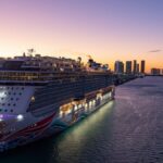 A luxury cruise ship docked in Miami Bay at sunset with city skyline views.
