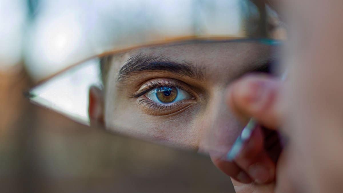 A striking portrait reflecting a blue eye in a piece of broken mirror outdoors.