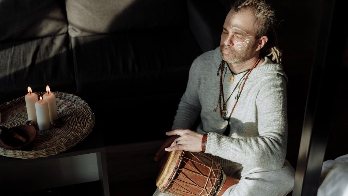 Man meditating indoors with a percussion instrument and candles, embracing tranquility.