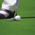A golf player prepares to hit a ball with a putter on a green course.