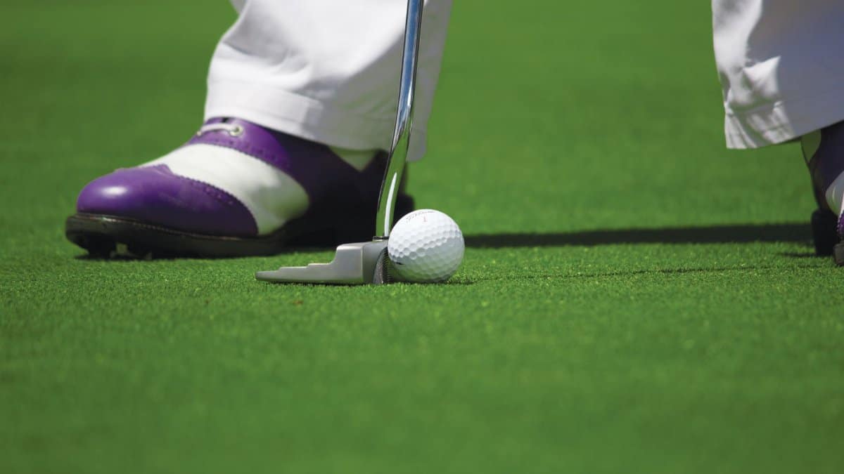 A golf player prepares to hit a ball with a putter on a green course.