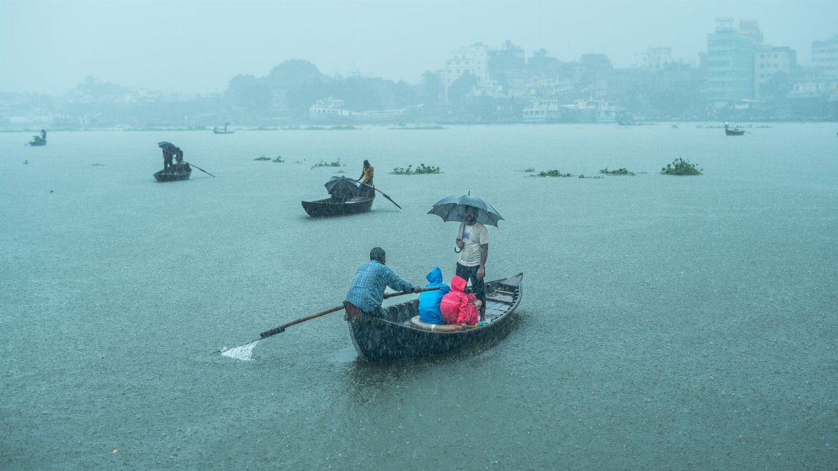 Scene of people in a boat crossing a river during rainfall, capturing daily life by water.
