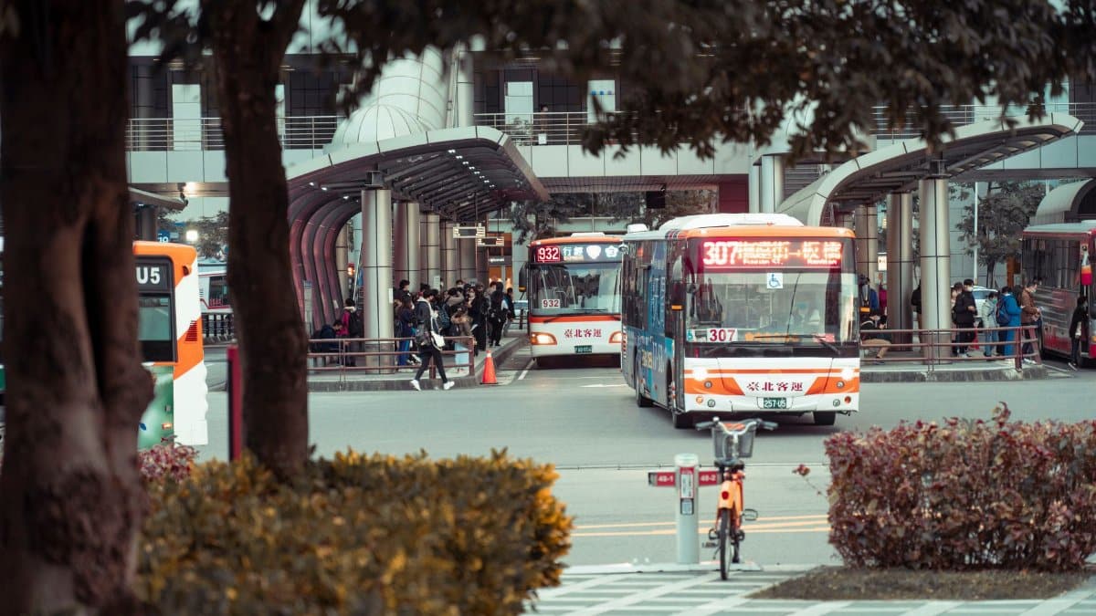 Crowded bus station with multiple buses and commuters in an urban setting.