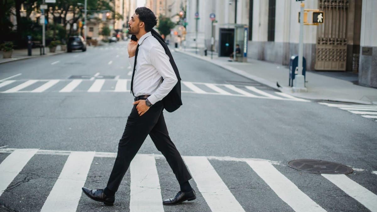 Confident businessman crossing city street holding jacket, urban professional style.