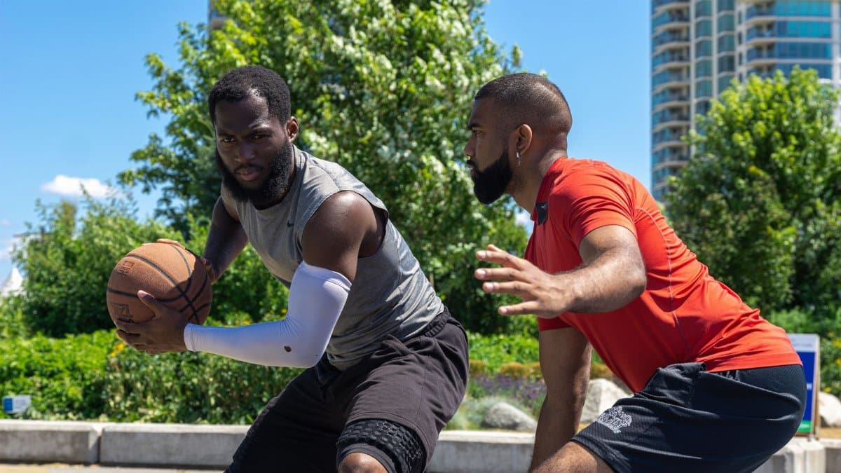 Two men playing a competitive basketball game outdoors on a sunny day.