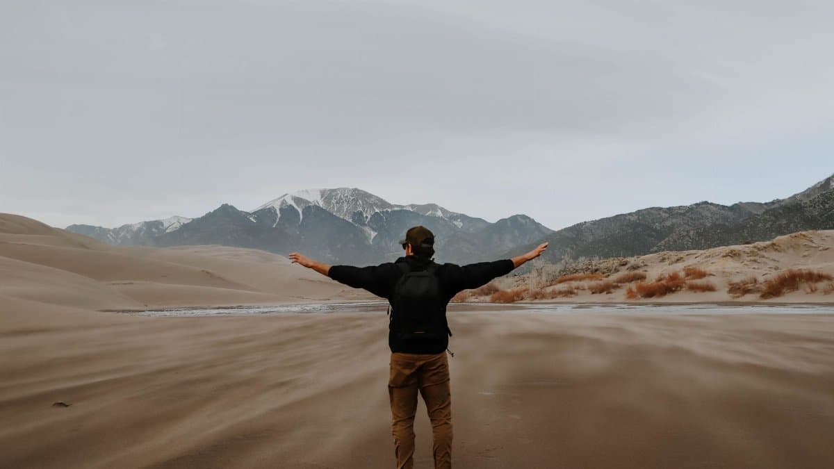 Man with backpack embracing desert scenery, showcasing adventure and freedom.