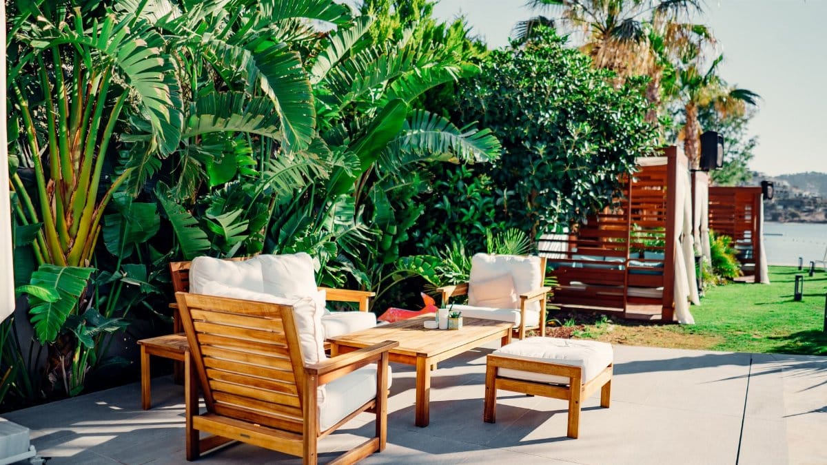 Relaxing outdoor patio with wooden furniture surrounded by lush greenery and tropical plants.