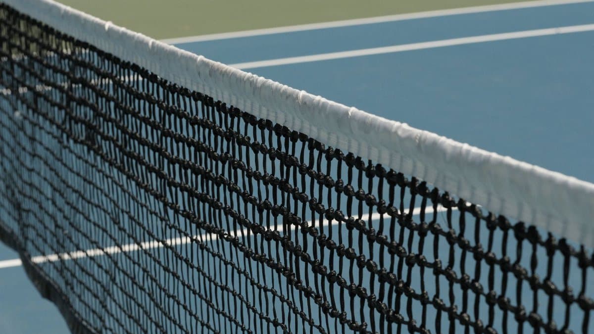 Detailed perspective of a tennis net casting shadows on a vibrant blue court under sunlight.