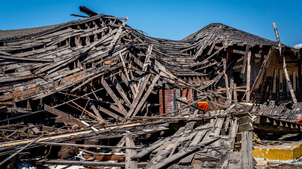 A dramatic view of a destroyed wooden building after a catastrophe, showing debris and structural failure.