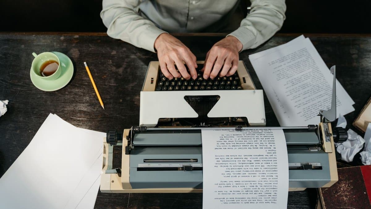 Hands typing on a vintage typewriter with papers and a coffee cup in view.