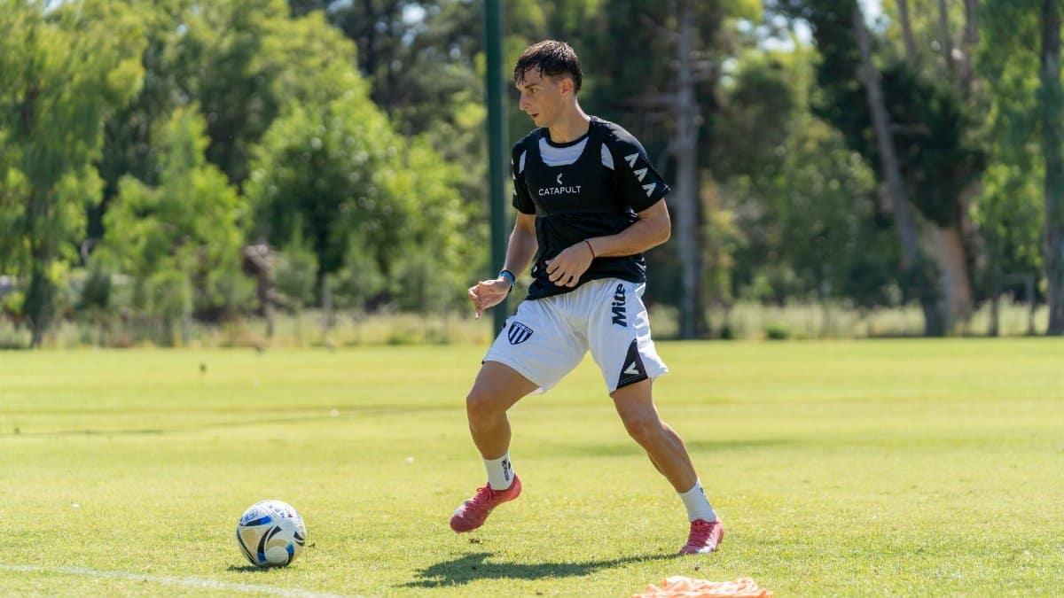 A young male soccer player in athletic gear practicing on a sunny day in a grassy field.