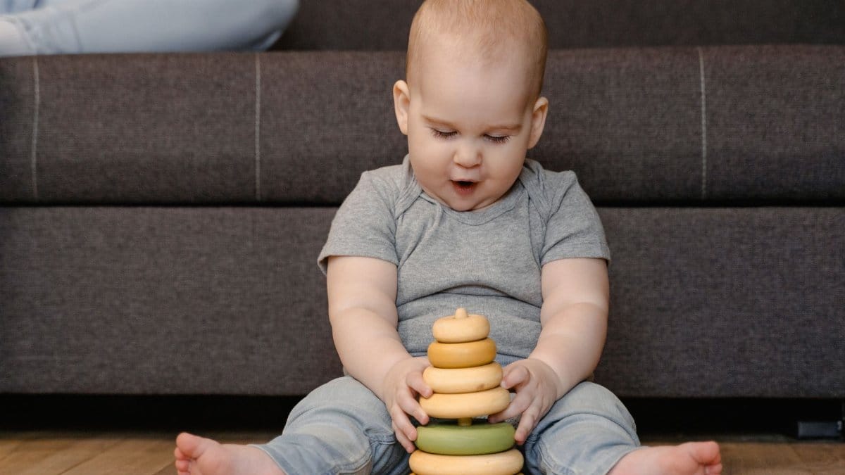 Adorable baby sitting on the floor, engaged with a colorful stacking toy in a cozy indoor setting.