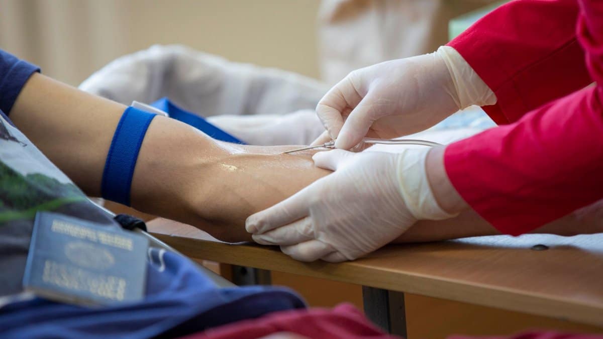 Medical professional drawing blood from donor's arm in a clinical setting.