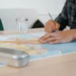 Student using a set square on a world map at a desk, taking notes indoors.
