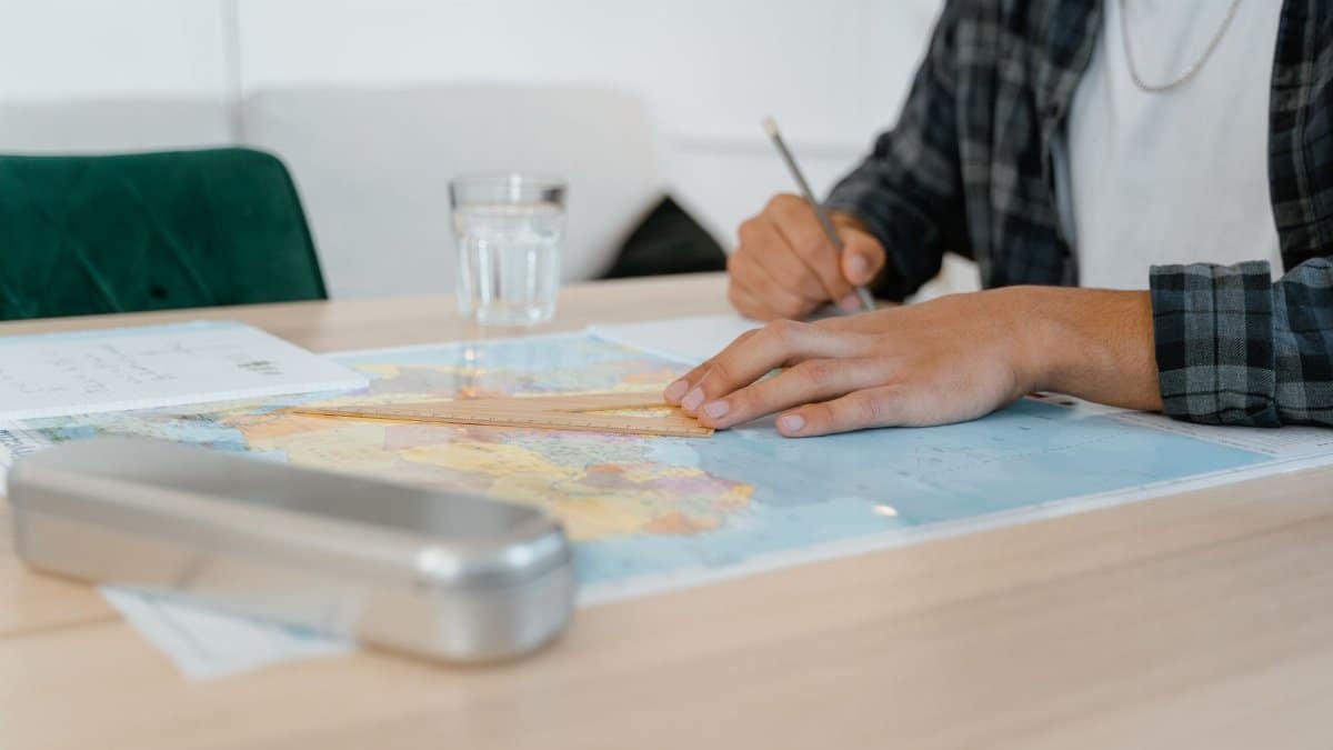 Student using a set square on a world map at a desk, taking notes indoors.