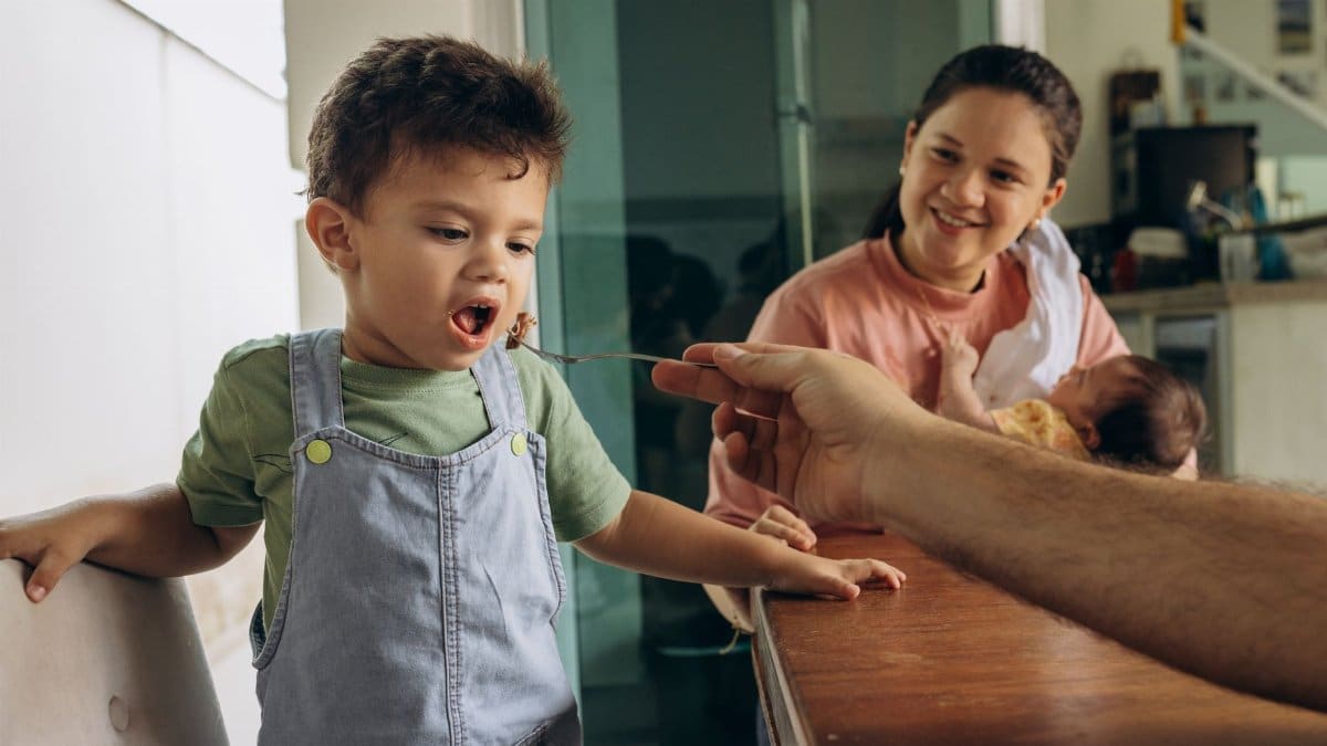Father feeding young son while mother holds newborn, capturing family interaction.