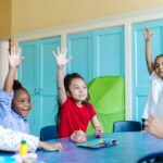 Children eagerly raising hands in a colorful classroom, engaged in learning.