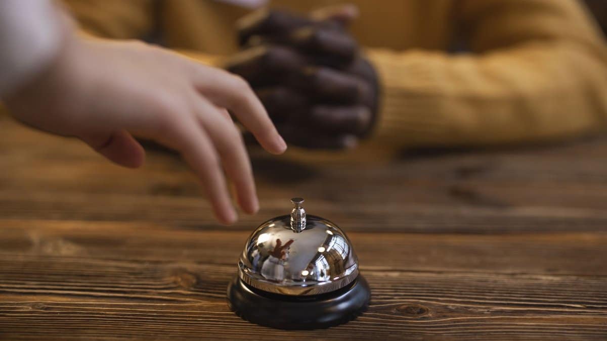 A hand reaching for a reception bell on a wooden table, indicating service or hospitality request.
