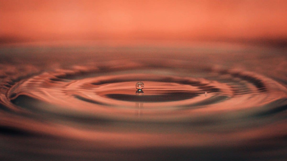 A captivating macro photograph capturing a single water droplet creating ripples on a calm water surface.