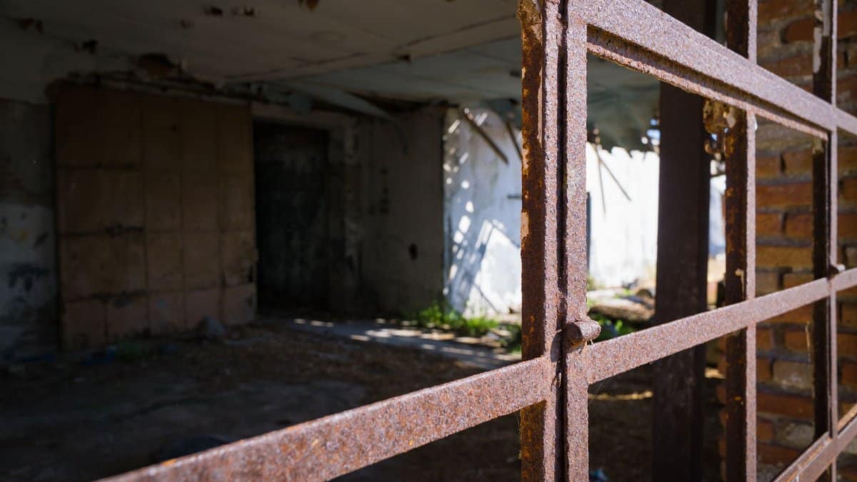 Rusty metal grate with light streaming into an abandoned dilapidated building.