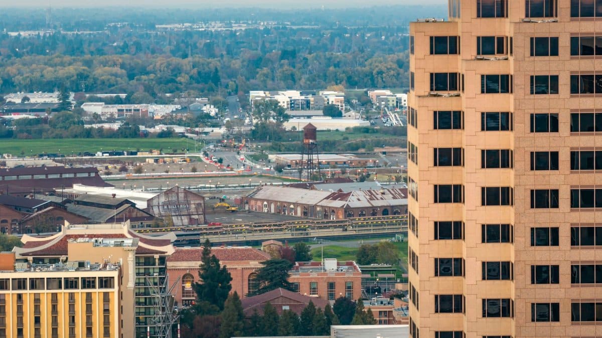 Detailed aerial view of Sacramento's urban landscape featuring diverse architecture and distant greenery in daylight.