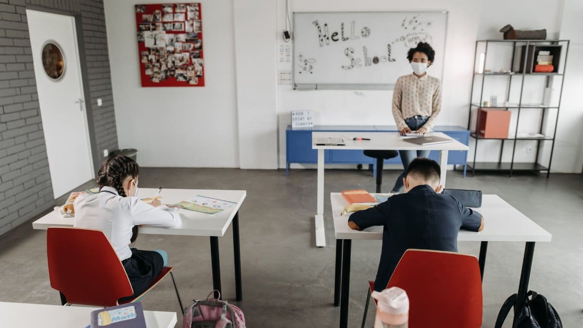 A classroom scene with children and a teacher wearing masks, a sign of new normal education.