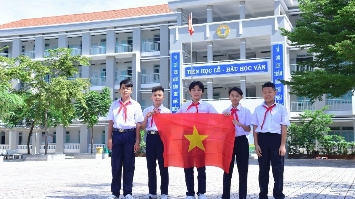 Group of Vietnamese students in school uniform proudly holding national flag in schoolyard.