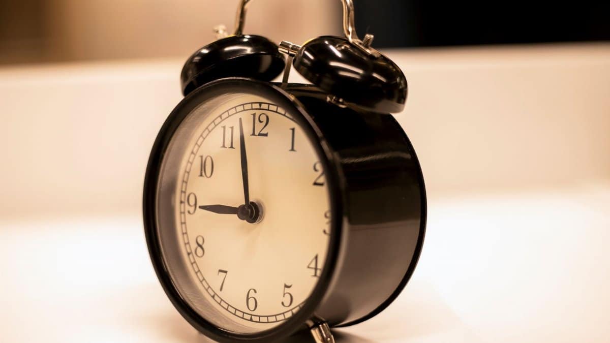 Close-up of a classic black analogue alarm clock on a desk with a serene background.