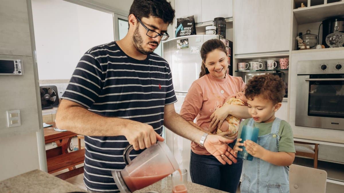 Family spending time in kitchen with father pouring juice for son and mother holding baby.