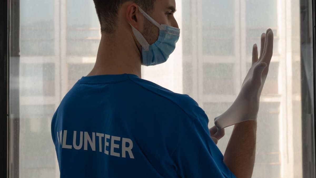 A masked volunteer putting on surgical gloves, exemplifying readiness for medical duty.
