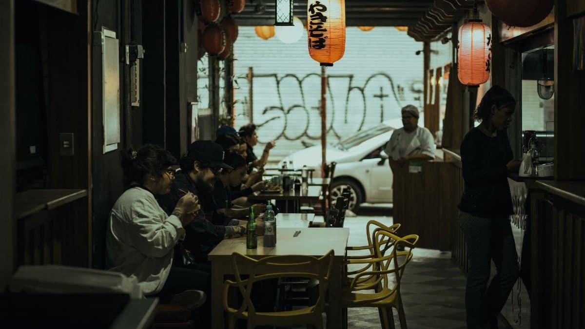 Dimly lit Asian restaurant interior with patrons enjoying dining under hanging lanterns.