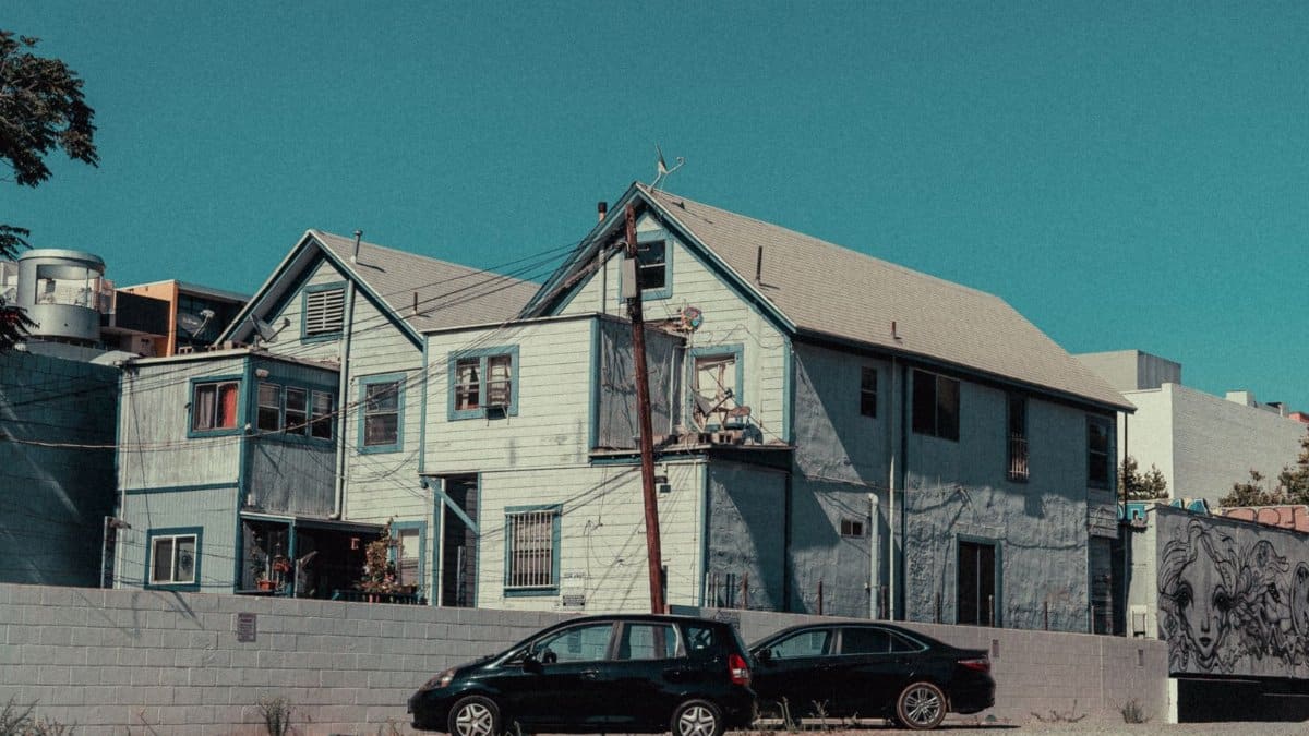 Grimey street view of residential houses and parked cars under a clear sky.