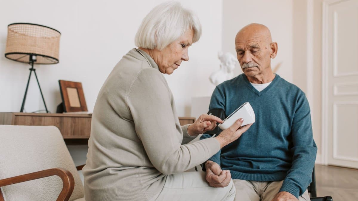 Elderly couple managing health by checking blood pressure at home, ensuring well-being.
