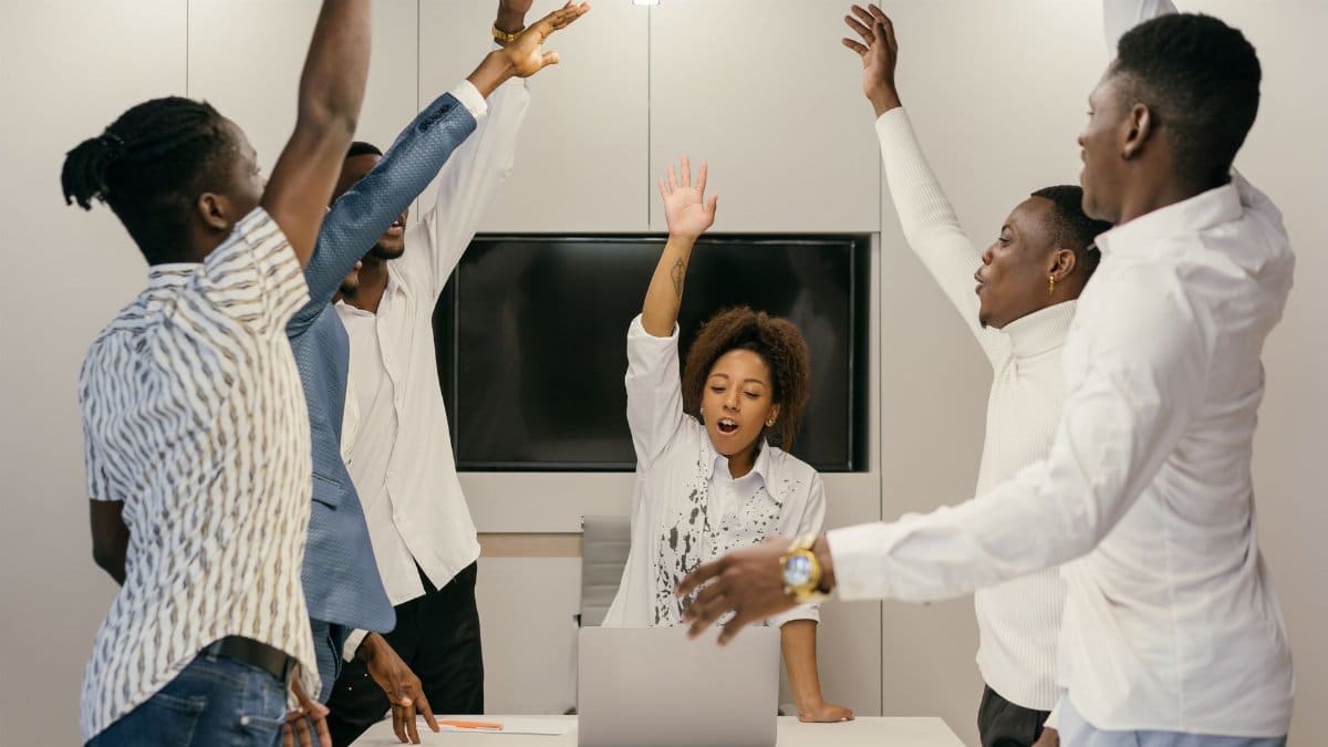 Group of diverse professionals raising hands during a collaborative team meeting in a modern office.
