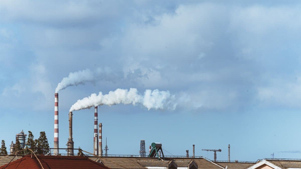 Factory chimneys emitting smoke over rooftops on a clear day, illustrating urban pollution.