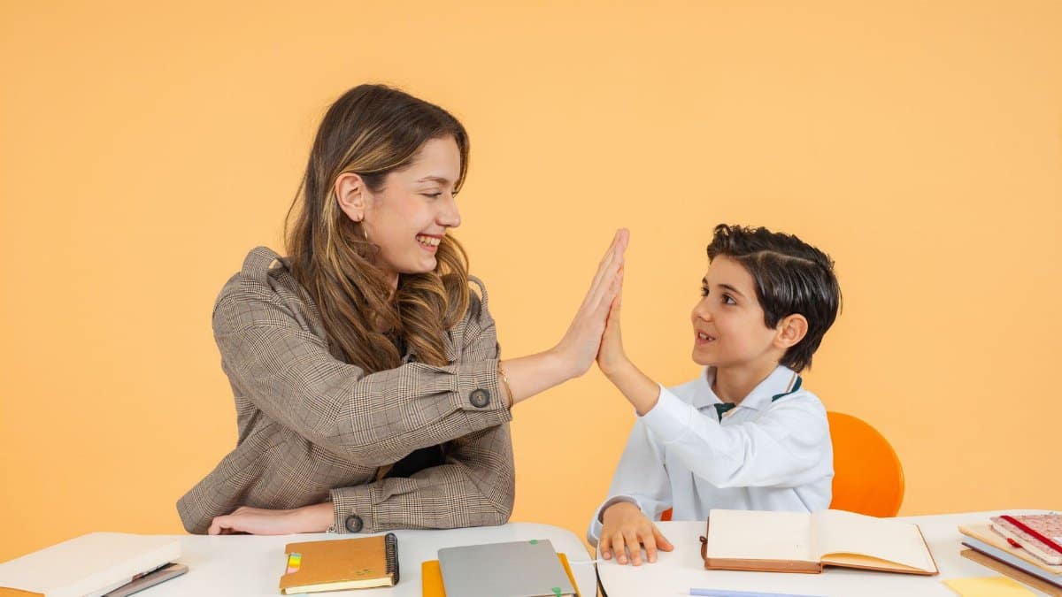 Teacher and student sharing a high-five over a desk in a bright classroom, fostering a positive learning environment.