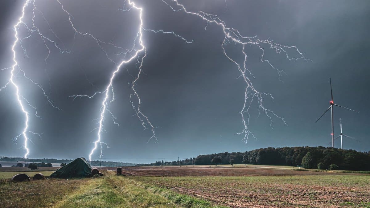 Vibrant lightning bolts illuminate a rural wind farm at night, creating a dramatic and powerful scene.