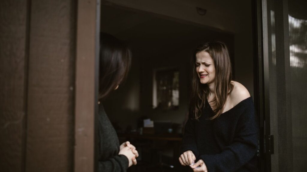A woman expressing emotions at a doorway, another person partially visible.