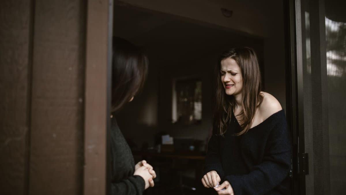 A woman expressing emotions at a doorway, another person partially visible.