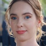 Close-up portrait of a young woman with blue eyes and natural makeup, shot outdoors.